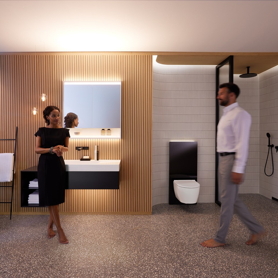 Mies ja nainen harmonisesti valaistussa kylpyhuoneessa, jossa on Geberit ONE -kylpyhuonekalusteet ja -posliinit (© Geberit)