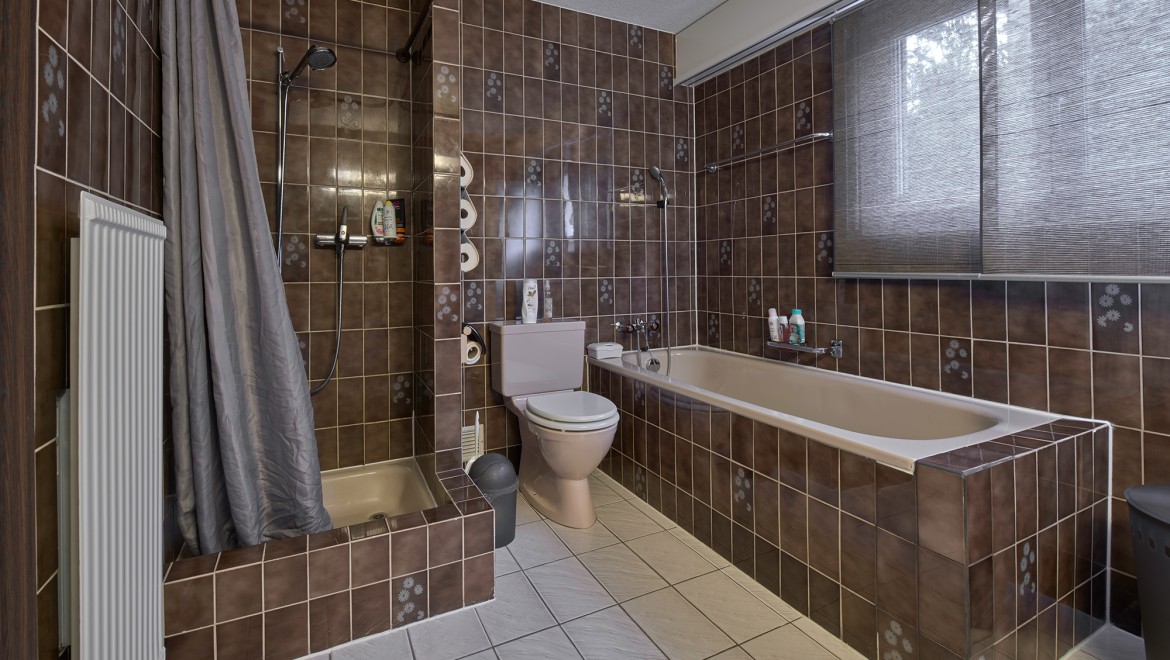 Kylpyhuone, jossa on kapea suihkunurkkaus, kylpyamme ja lattiamallinen WC-istuin